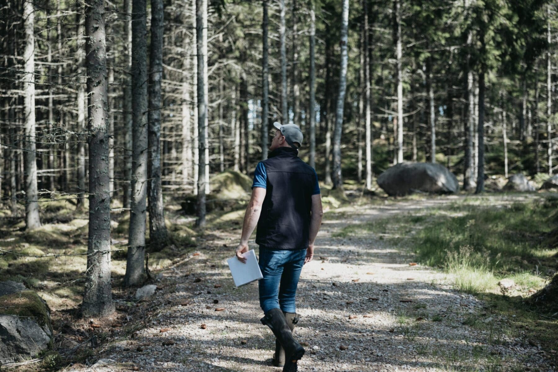 VIrkesinköpare på skogsbilväg med block i handen, inspekterar skogen för skogsrådgivning och skogsskötsel