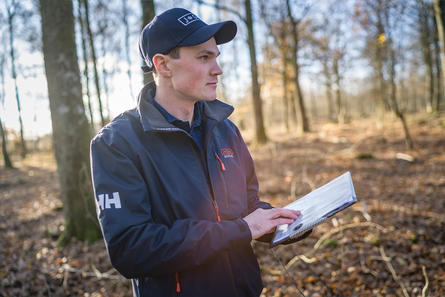 Inköpare i skog med skogsbruksplan i handen som ser ut över skogsområdet