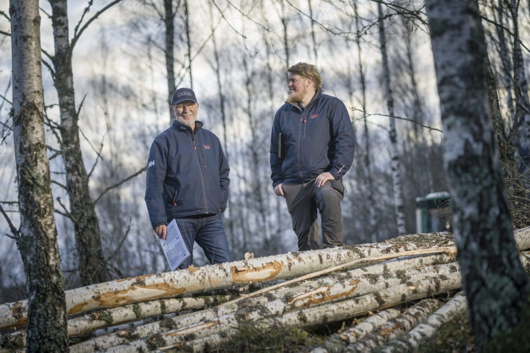 Virkesinköpare i skogen vid en trave björkstockar.